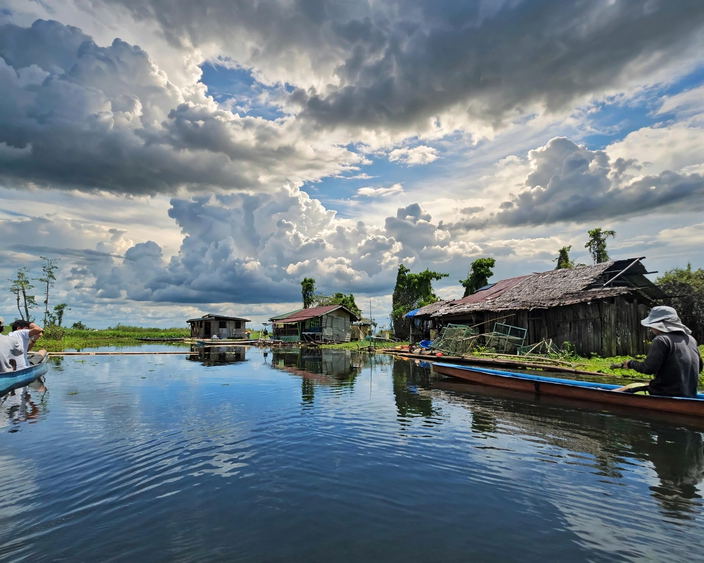 Wooden floating houses and outrigger boats on the still water of Lake Panlabuhan in the Agusan Marsh under a cloudy sky