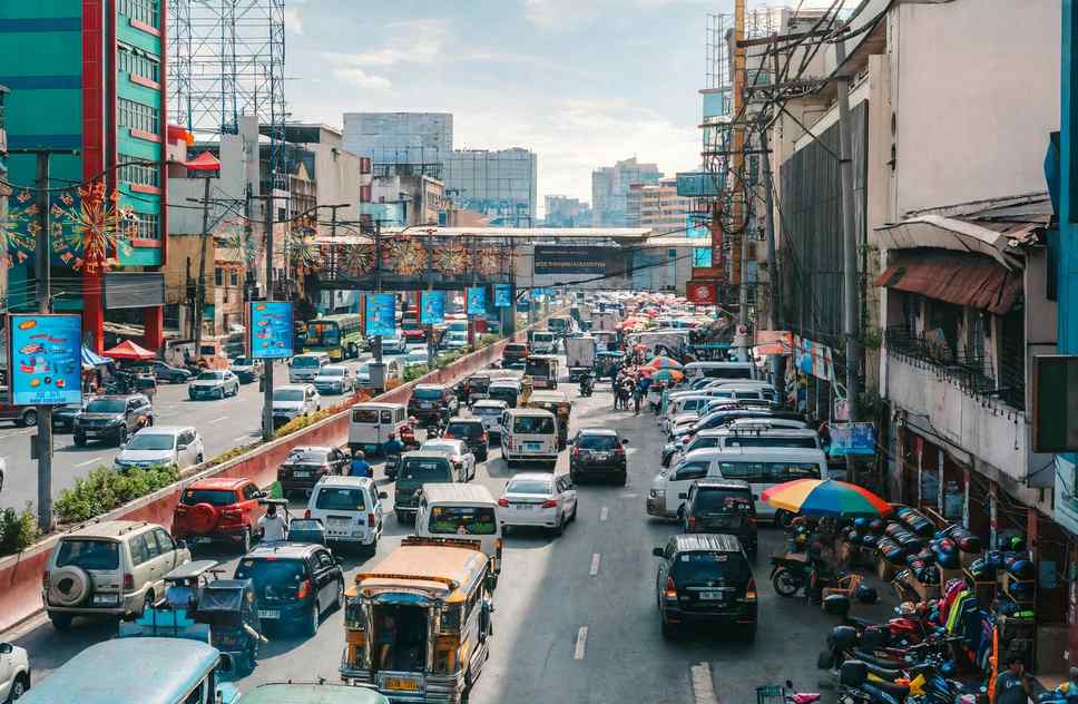 Heavy Manila traffic with jeepneys, vans and cars under a pedestrian overpass on a busy city road