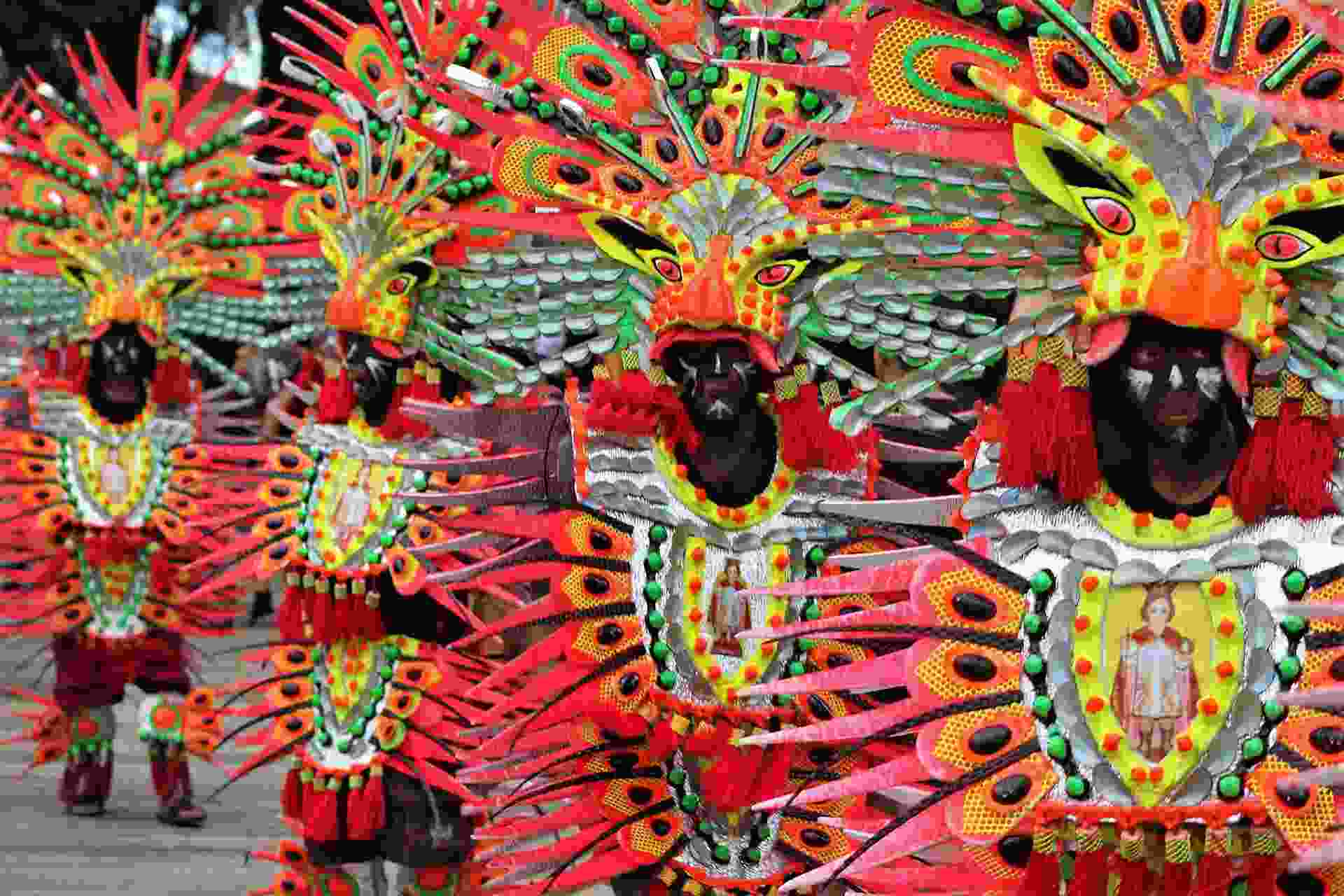 Festival dancers in colourful feathered headdresses and costumes decorated with a Santo Niño image
