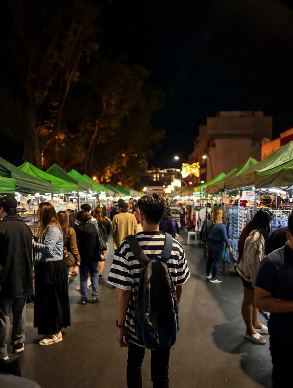 Shoppers in jackets walking between rows of green tents at the Baguio Night Market on Harrison Road, with clothing racks lit up on both sides
