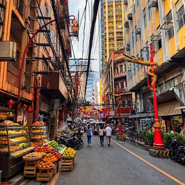 Narrow Binondo street with red lanterns, golden dragon posts and a fruit and bakery stall on the left