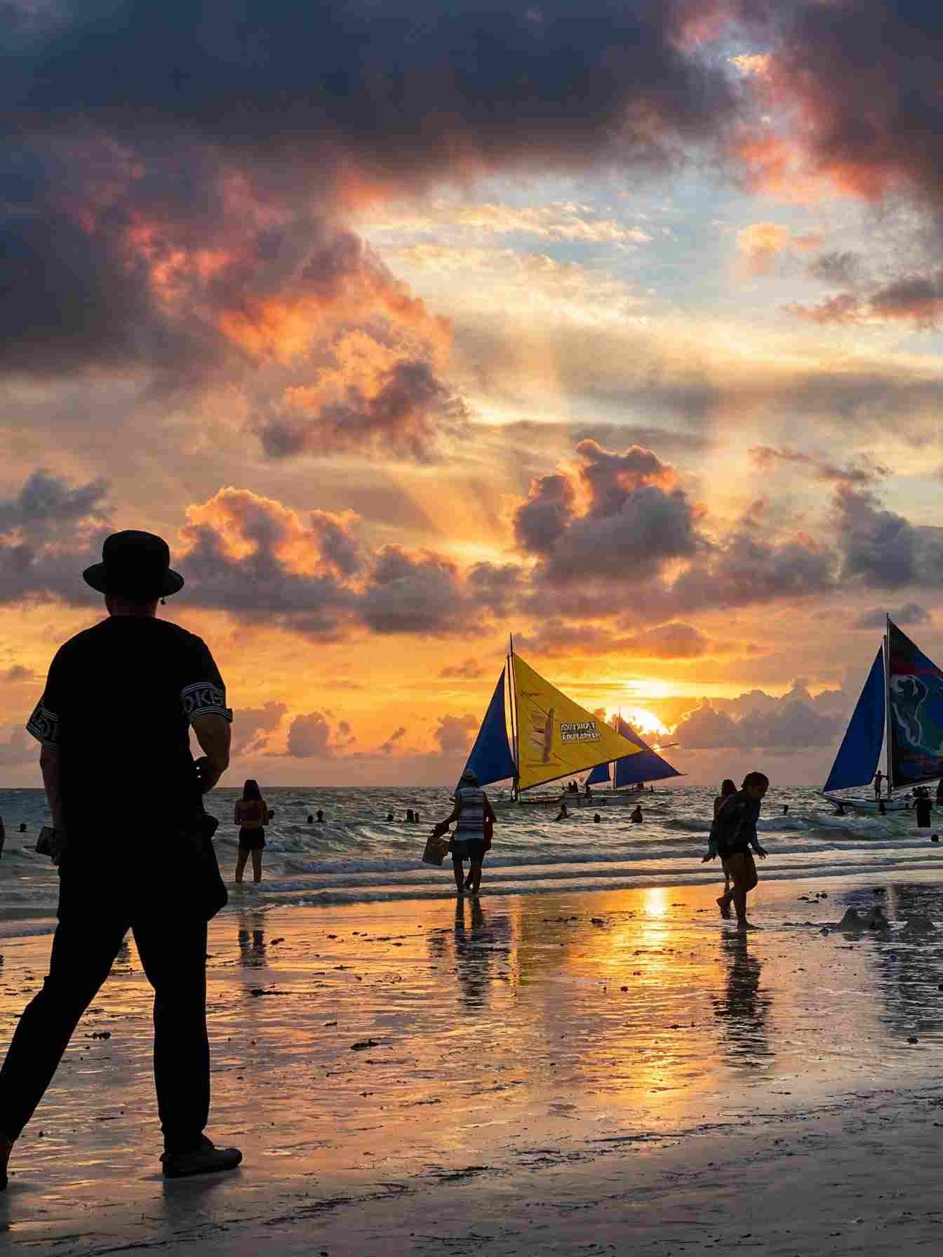 Silhouetted visitors on White Beach in Boracay with colourful paraw sailboats against an orange sunset sky