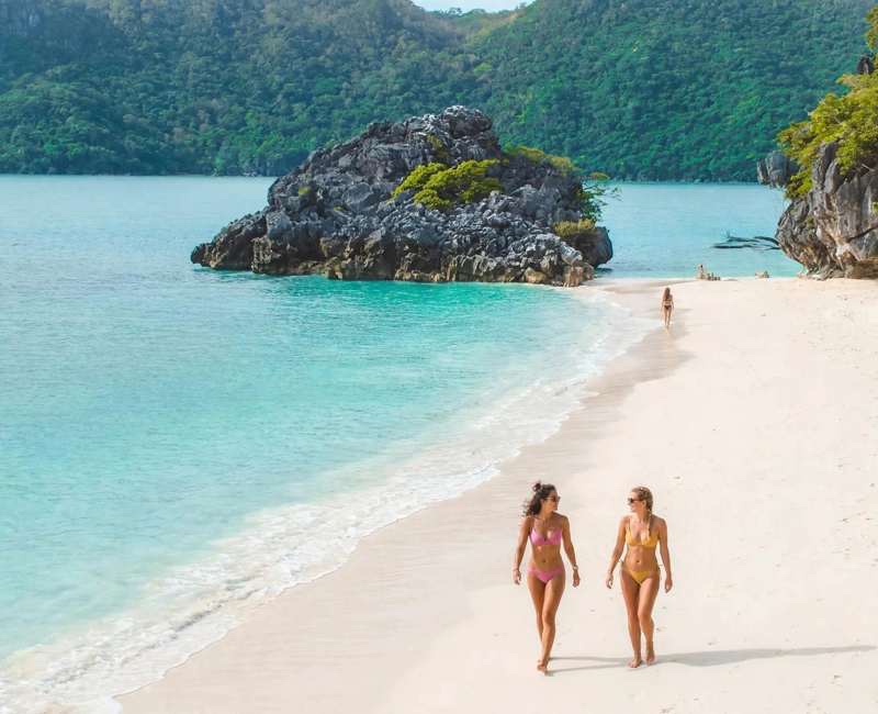 White-sand beach in the Caramoan Islands with a limestone rock islet, green hills and turquoise water
