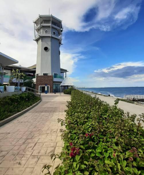 White lighthouse tower beside a paved seaside walkway and flowering hedge at IL Corso, South Road Properties, Cebu City