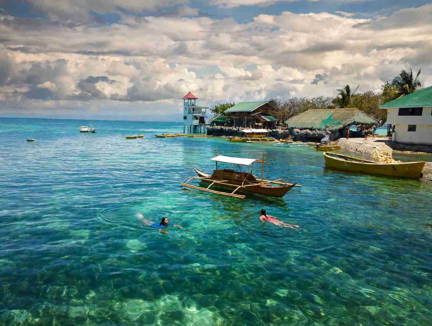 Swimmers and outrigger boats in clear water at an island stop off Cordova, Cebu