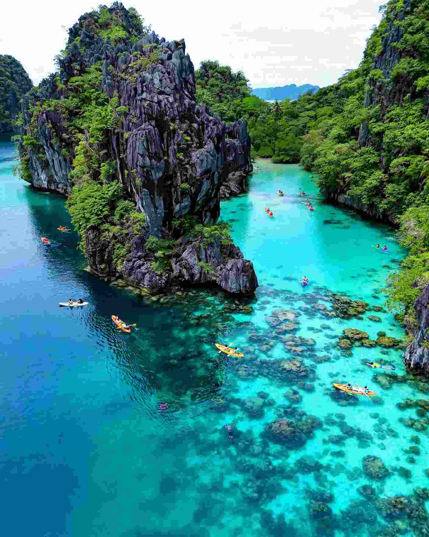 Kayaks and swimmers in a turquoise lagoon between limestone cliffs near El Nido, Palawan