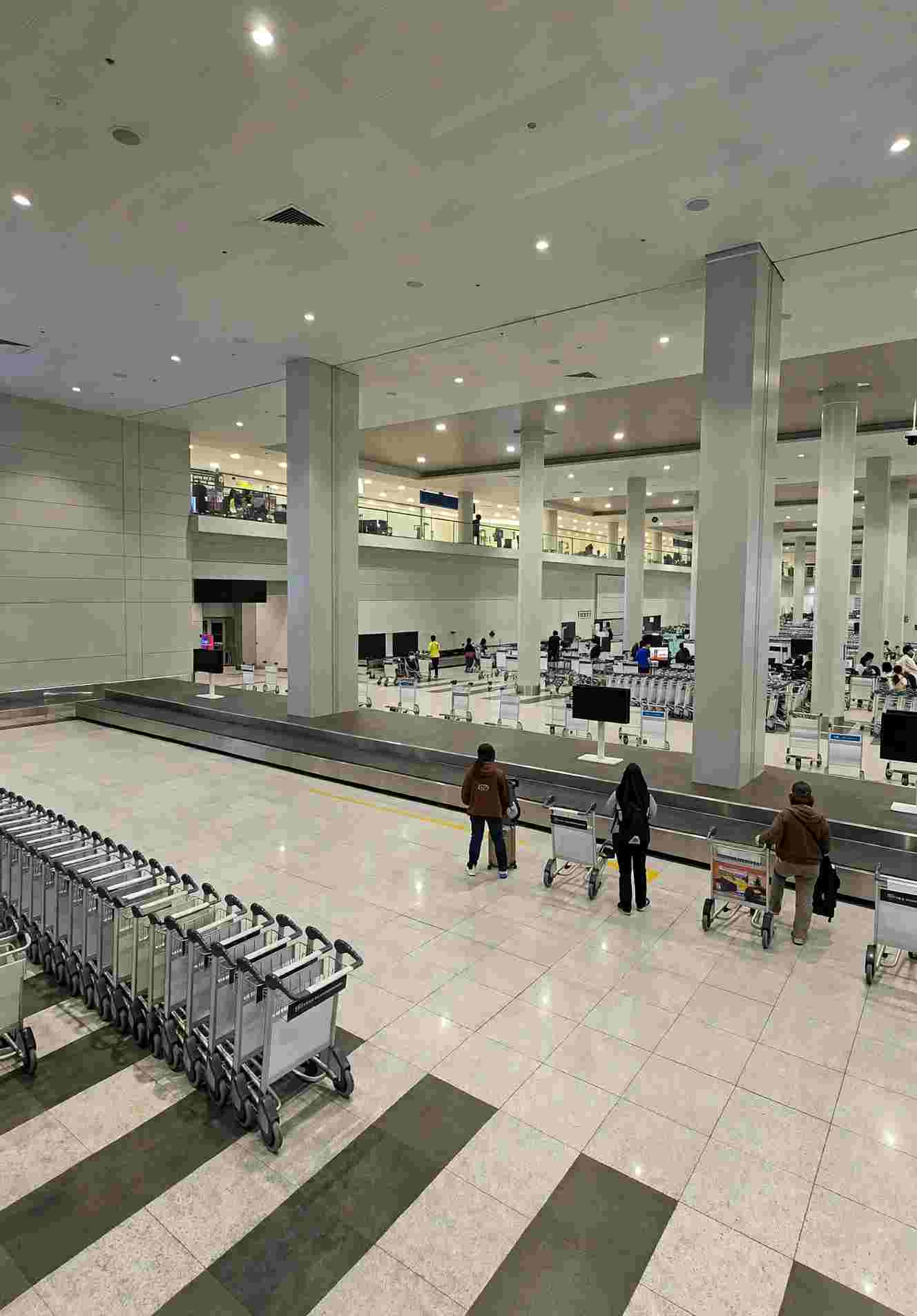 Baggage claim hall inside NAIA airport in Manila, with rows of luggage carts, a carousel belt and travelers walking across the tiled floor
