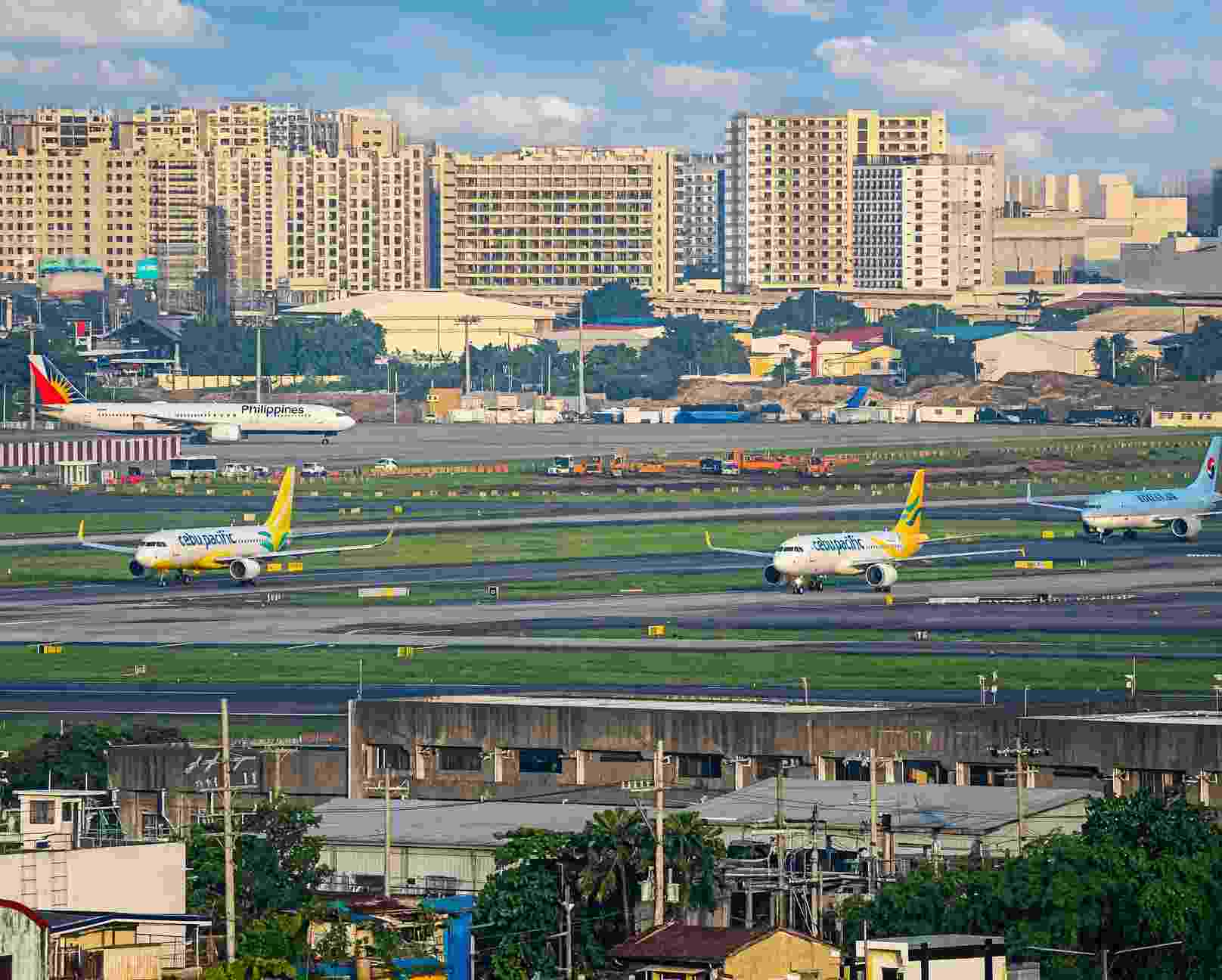 Cebu Pacific and Philippine Airlines jets on the taxiways at Manila's airport with apartment towers behind