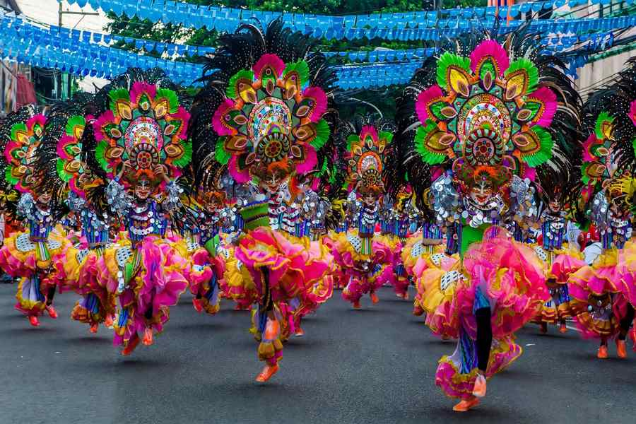 MassKara Festival dancers in smiling masks and feathered headdresses on a Bacolod street