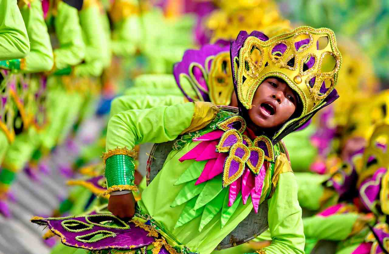 Sandugo street dancer in a lime-green costume and gold-trimmed purple headdress mid-routine, with a line of dancers blurred behind